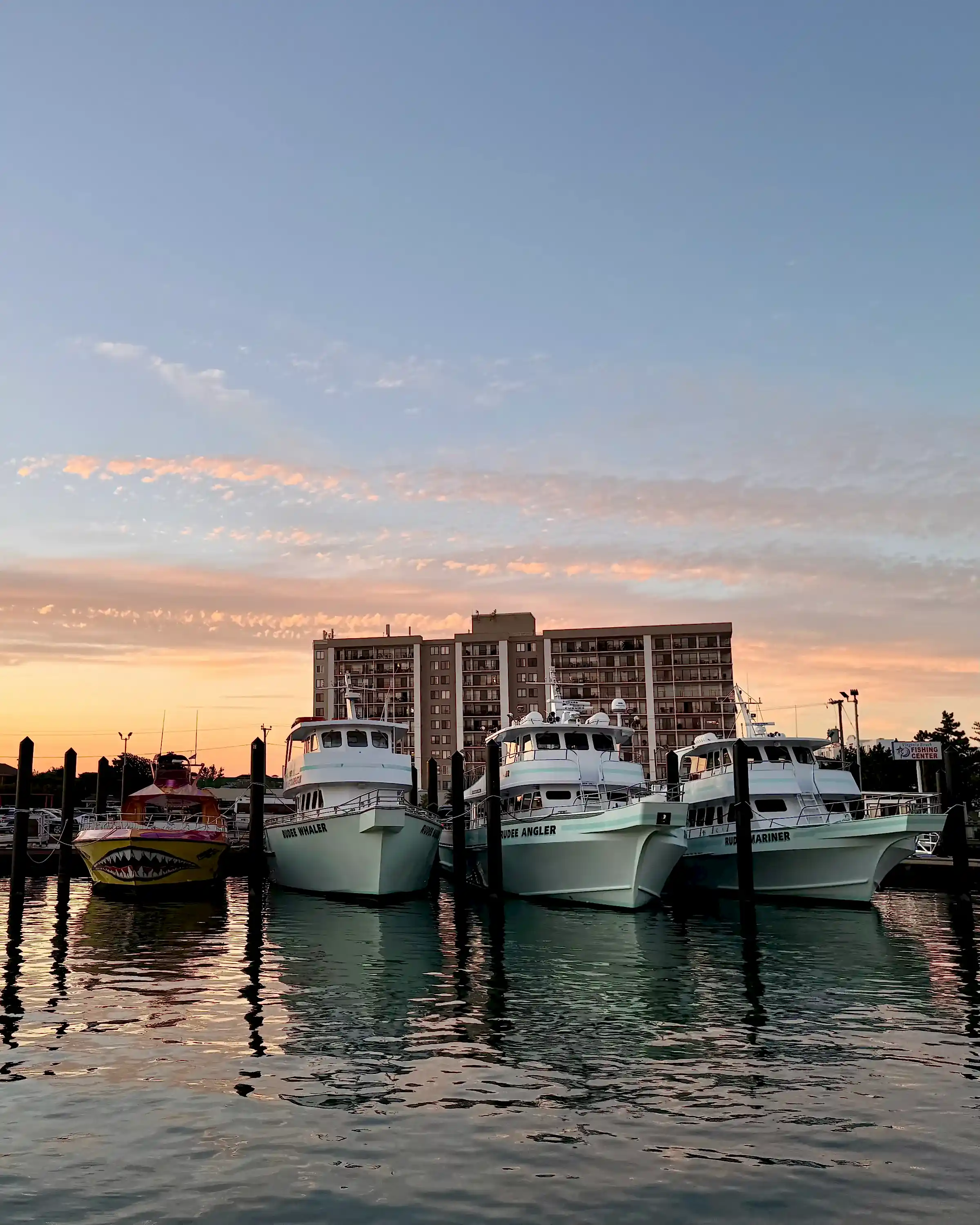 Boats docked at sunset with a building in the background and colorful sky.