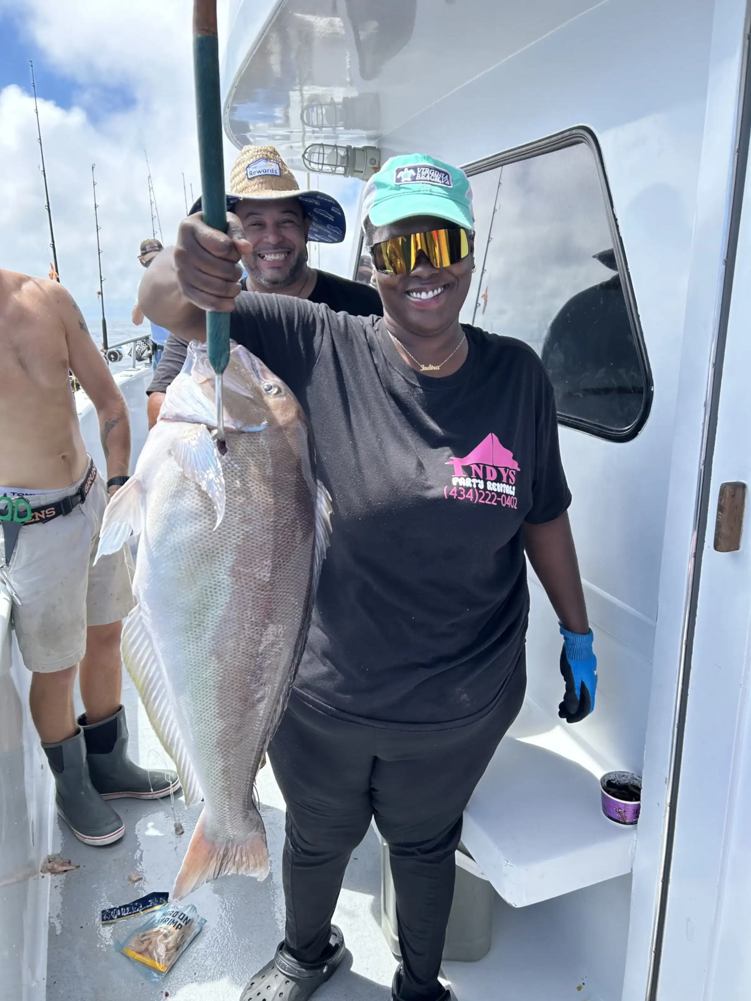Smiling person on a boat holding a large fish with others in the background.